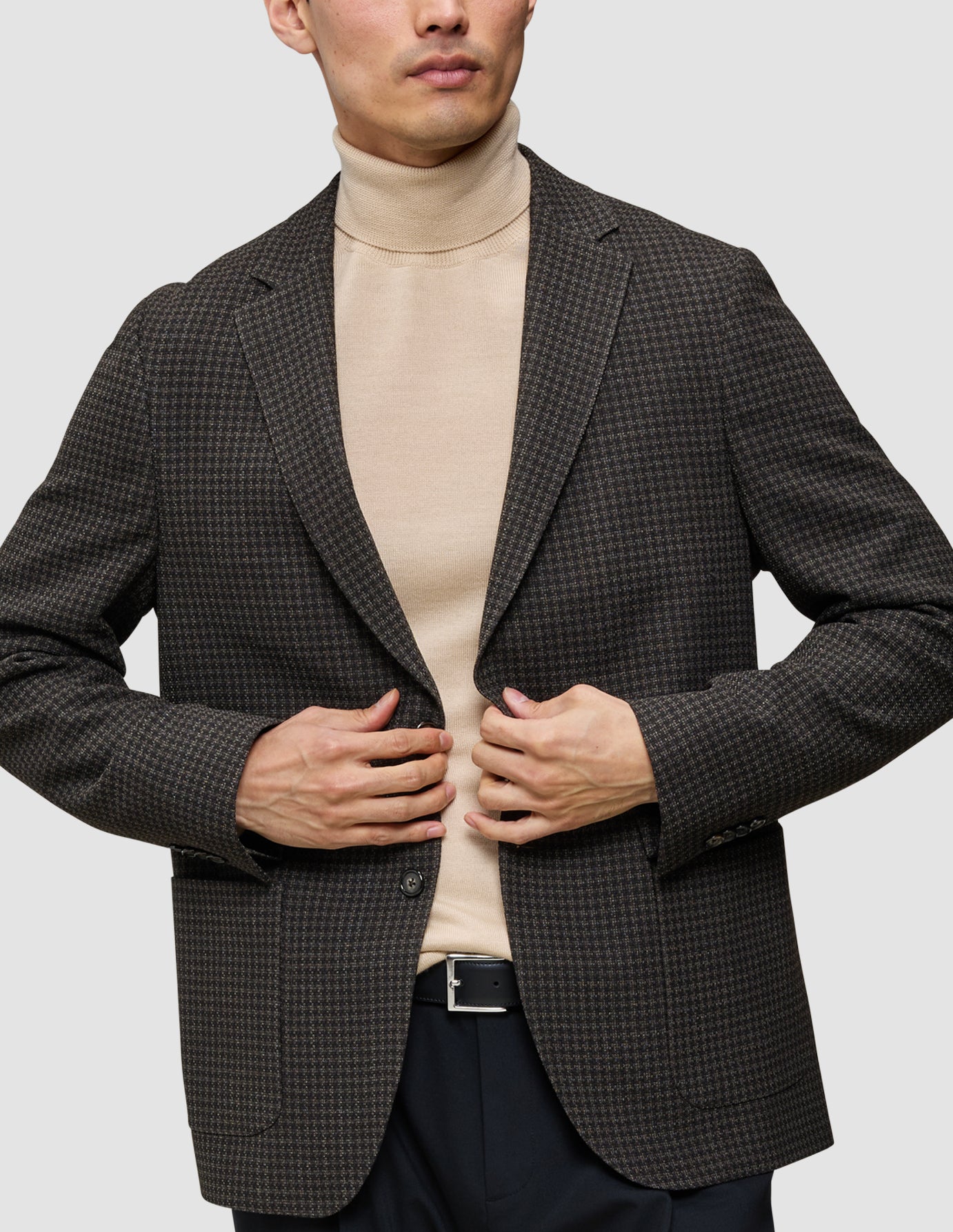 A person wears the knit-and-blazer look, featuring a merino crewneck sweater under a dark brown patterned wool blazer.
