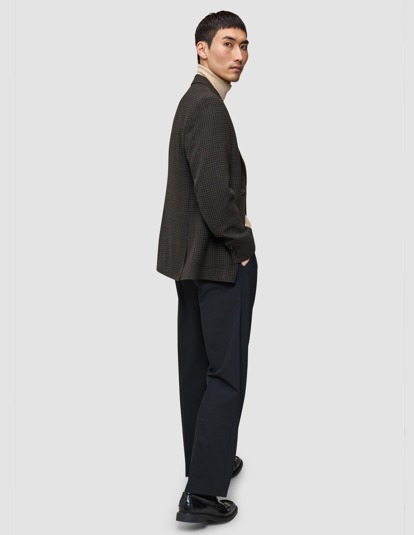 A man wearing The knit-and-blazer look consisting of a tan merino crewneck, a dark patterned wool blazer, and dark trousers.