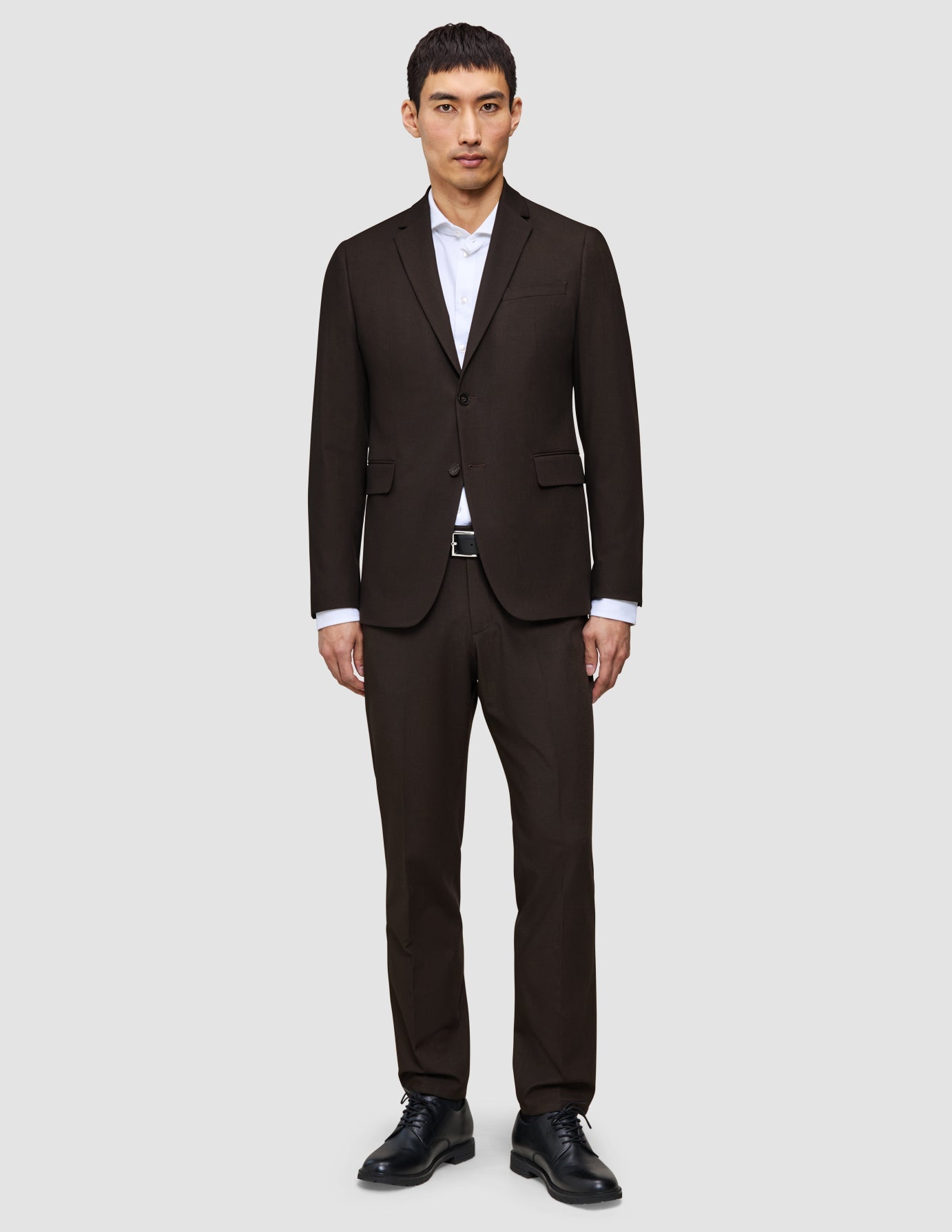 A man wears The suit that does it all in dark brown over a white button-down shirt and black dress shoes.