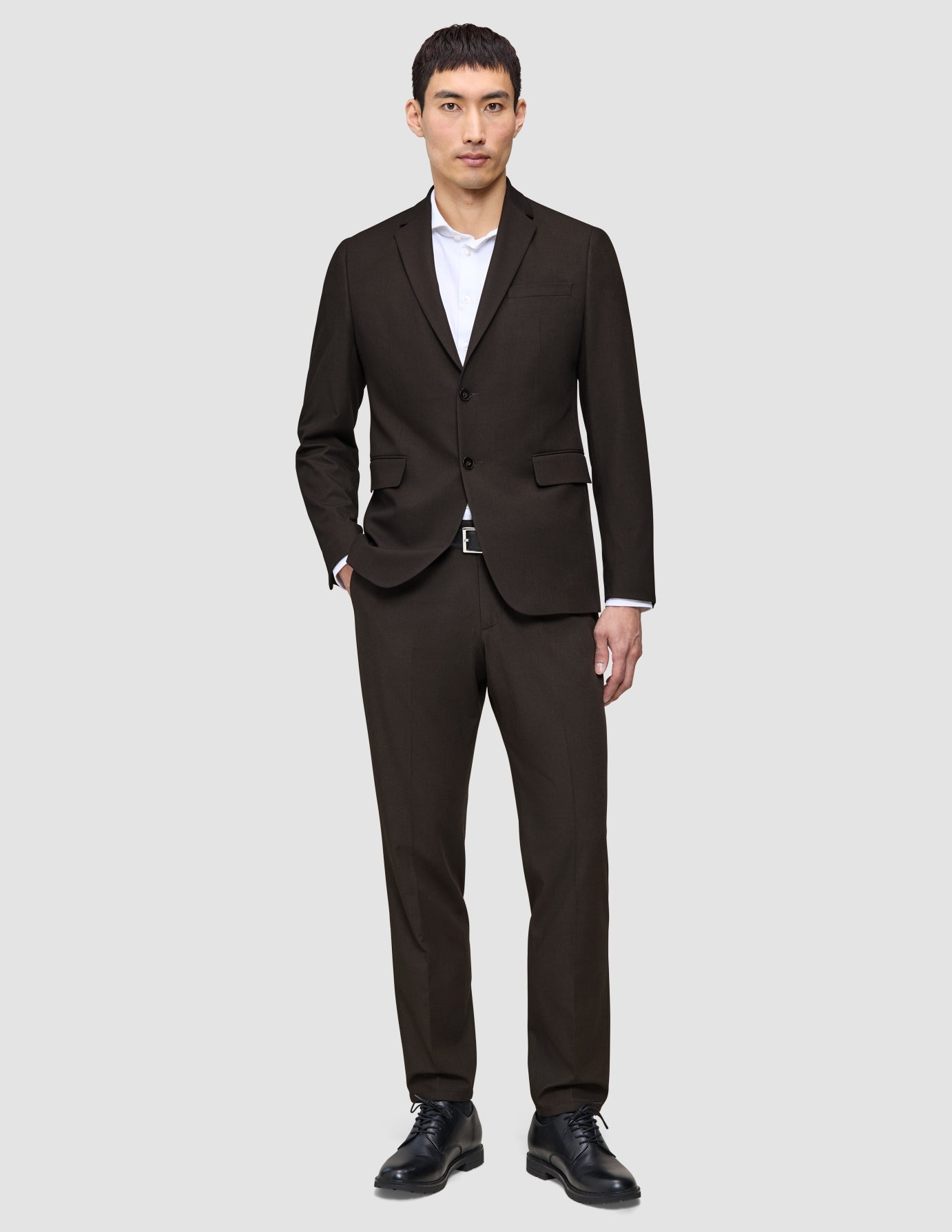 A man wearing The suit that does it all in dark brown, paired with a white dress shirt and black leather shoes.