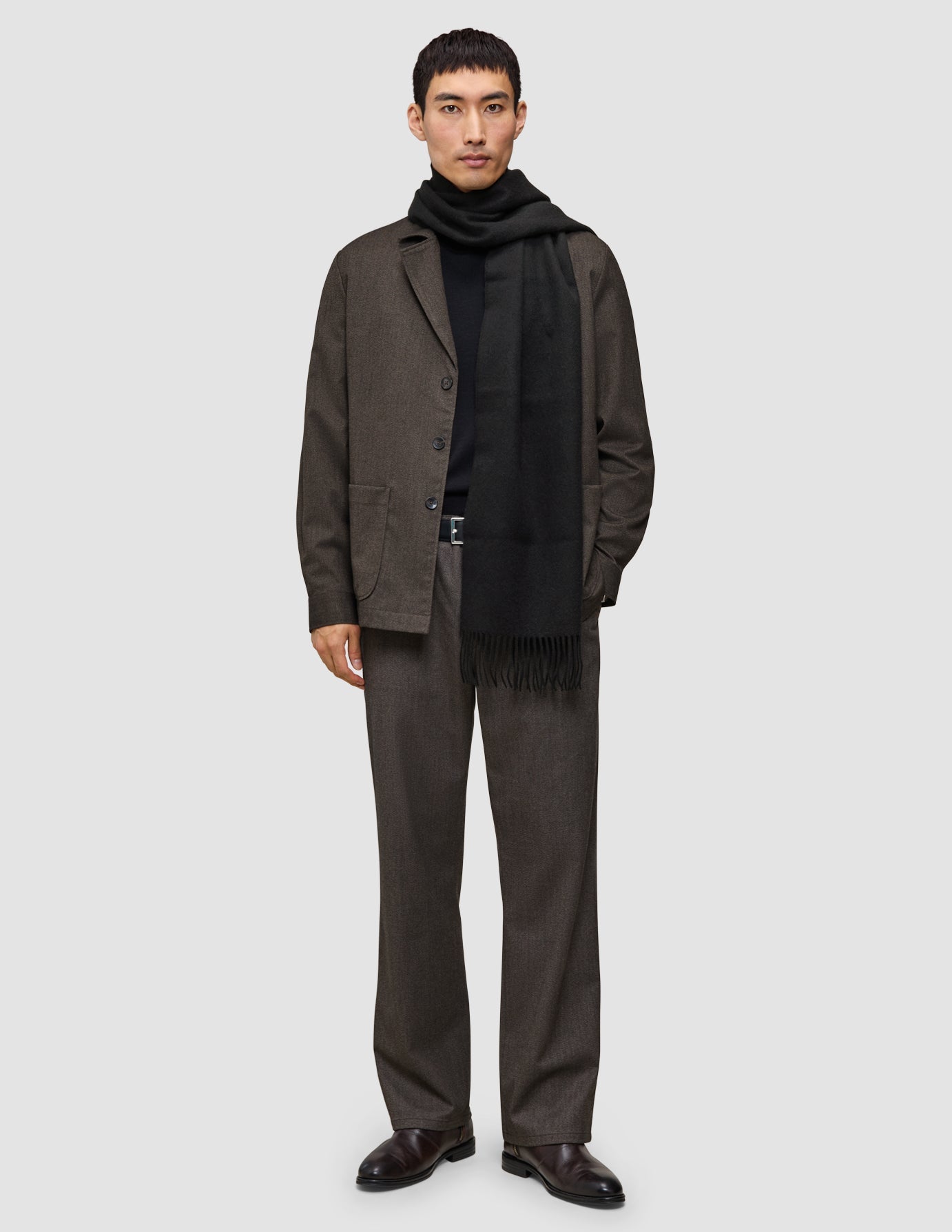 A man wearing A different kind of suit consisting of Atelier Pants and a dark brown Atelier Overshirt over a black turtleneck and black scarf.