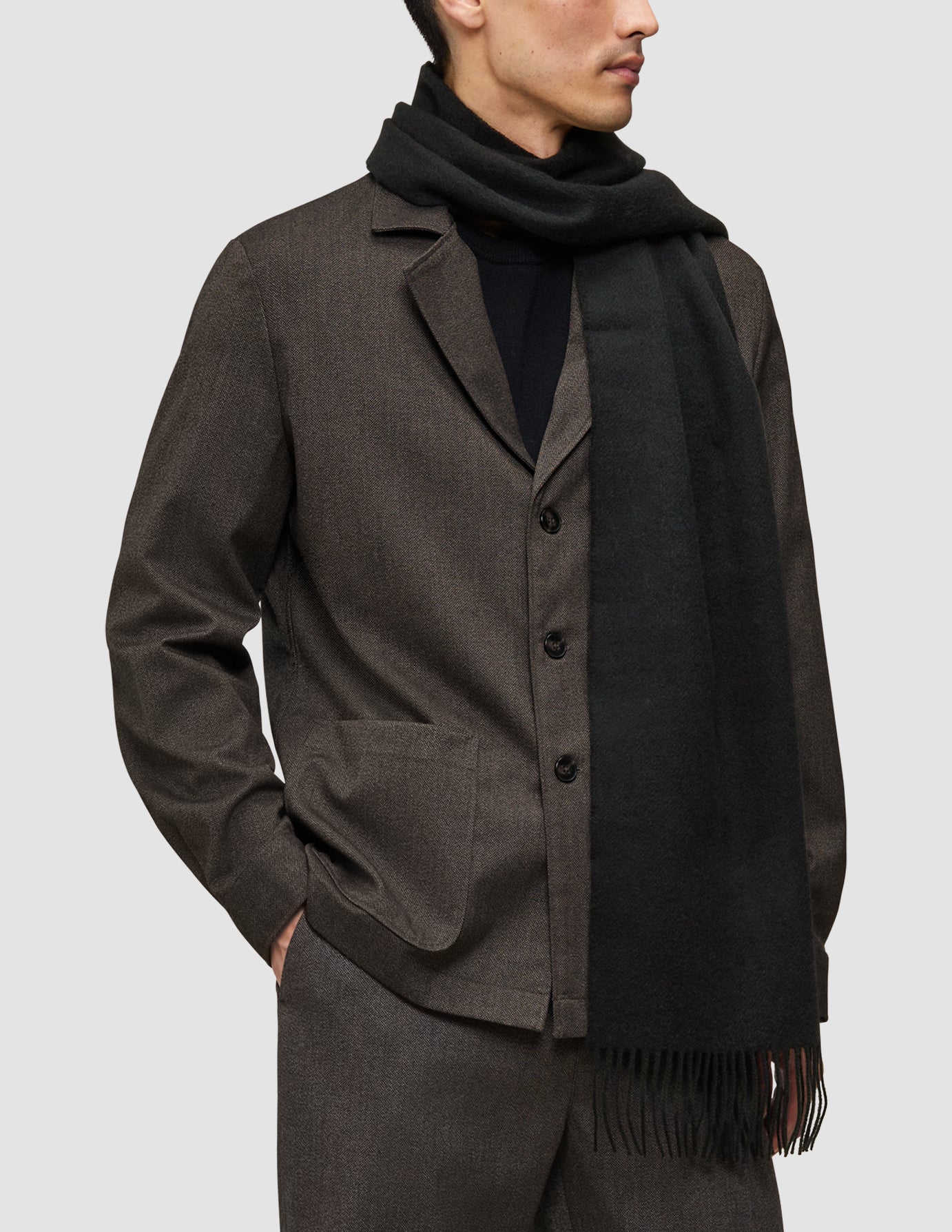 A person wearing a brown A different kind of suit over a black Merino Knit sweater and a long black fringed scarf.