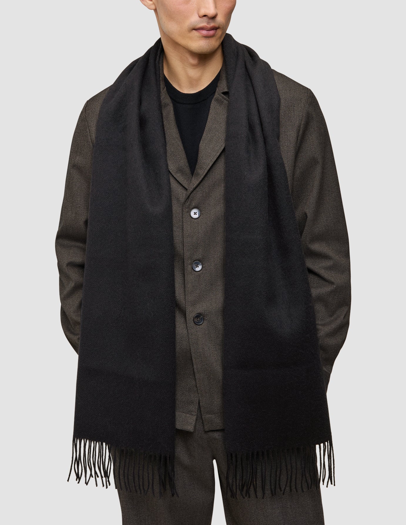 A man wearing an A different kind of suit, a dark brown Atelier Overshirt, and a long black scarf with fringed ends.