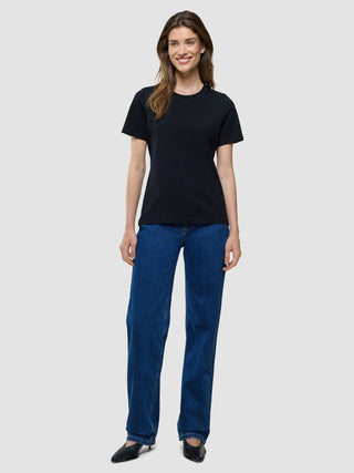 A smiling woman wearing a Supima T-shirt Black and blue jeans.