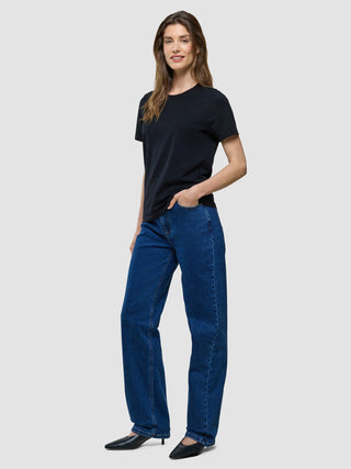 A smiling woman wearing a Supima T-shirt Black and blue jeans.