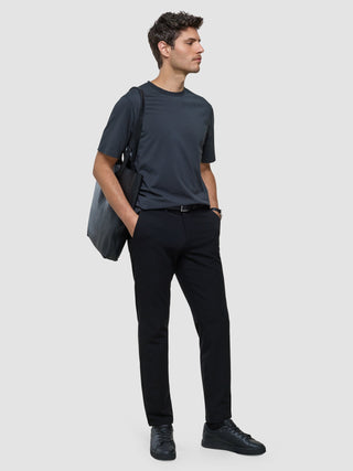 A man in a Supima T-shirt Box Fit Deep Grey, black trousers, and black sneakers, carrying a black tote bag over his shoulder.