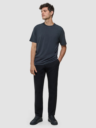 A man wearing a Supima T-shirt Box Fit Deep Grey, black trousers, and black sneakers featuring 360° stretch.