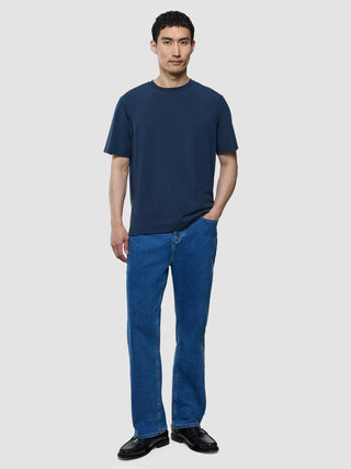 A man wearing a Supima T-shirt Box Fit Navy and blue jeans, standing with his hand in his pocket.