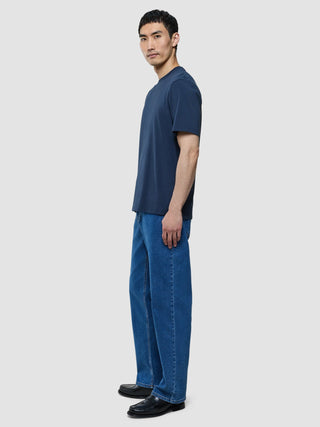 A man in profile wearing a Supima T-shirt Box Fit Navy, blue jeans, and black loafers in a clean Scandinavian design.