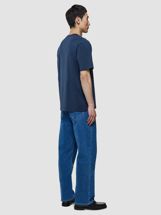 A man seen from the side wearing a Supima T-shirt Box Fit Navy and blue jeans.