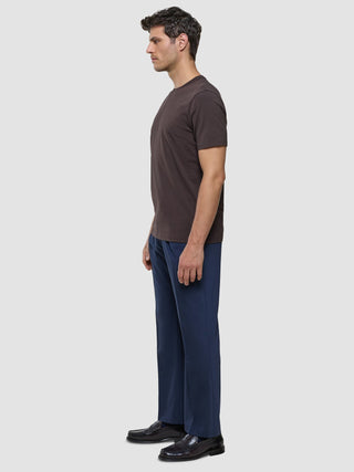 A man in profile wearing a Supima T-shirt Deep Brown, blue trousers, and loafers.