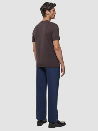 A man seen from behind wearing a Supima T-shirt Deep Brown, blue trousers, and dark loafers designed with 360° stretch.