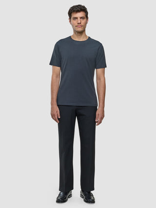 A man wearing a Supima T-shirt Deep Grey, dark trousers with 360° stretch, and black loafers stands against a plain background.