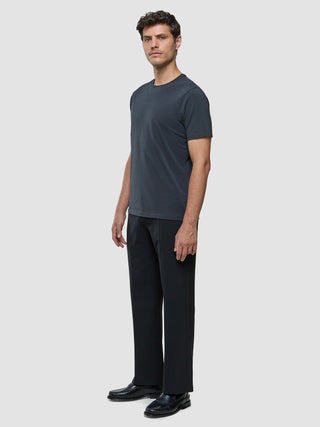 A man wearing a Supima T-shirt Deep Grey, black trousers, and black loafers designed with Scandinavian minimalism.