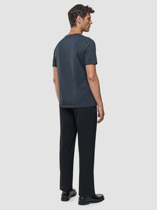 A man seen from behind wearing a Supima T-shirt Deep Grey, black trousers, and black loafers designed with 360° stretch.