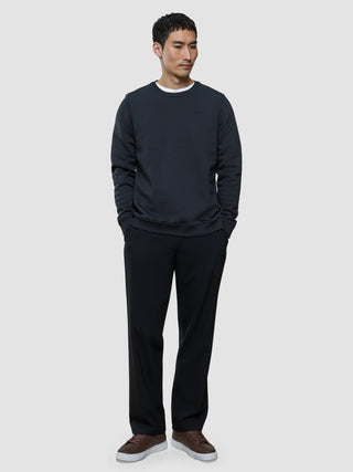 A man wearing a Sweat Crewneck Deep Grey over a white t-shirt, black trousers, and brown sneakers.