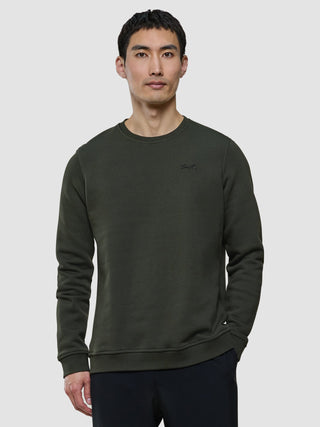 A man wearing a Sweat Crewneck Green Night with Snt. embroidered on the chest.