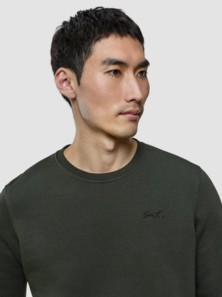A man wearing a Sweat Crewneck Green Night with Snt. embroidered on the chest.