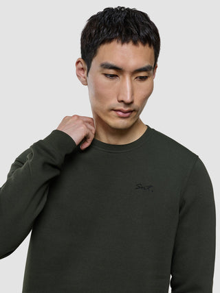 A man looks down wearing a Sweat Crewneck Green Night with Snt. embroidered on the chest.