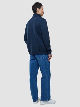 A person seen from behind wearing a Sweat Half Zip Dark Navy, blue jeans, and white sneakers.