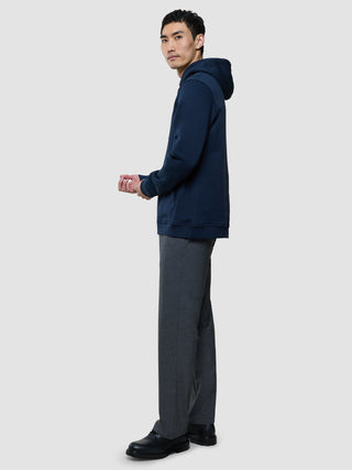 A man standing in profile wearing a Sweat Hoodie Dark Navy, grey trousers, and black shoes.