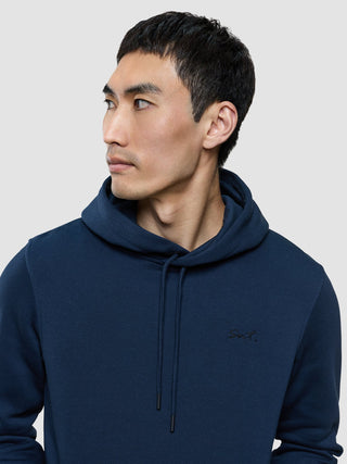 A man wearing a Sweat Hoodie Dark Navy with Snt. embroidered on the chest, showcasing a minimalist Scandinavian design.