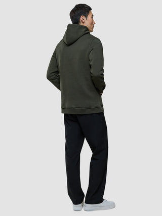 A man seen from behind wearing a Sweat Hoodie Green Night, black trousers, and white sneakers.