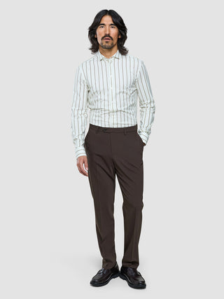 A man wearing a white and brown striped button-down shirt and Tech Wool Suit Pants Regular Cocoa Brown with dark loafers.