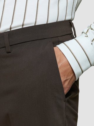 A person wearing Tech Wool Suit Pants Regular Cocoa Brown and a white striped shirt with their hand in a trouser pocket.