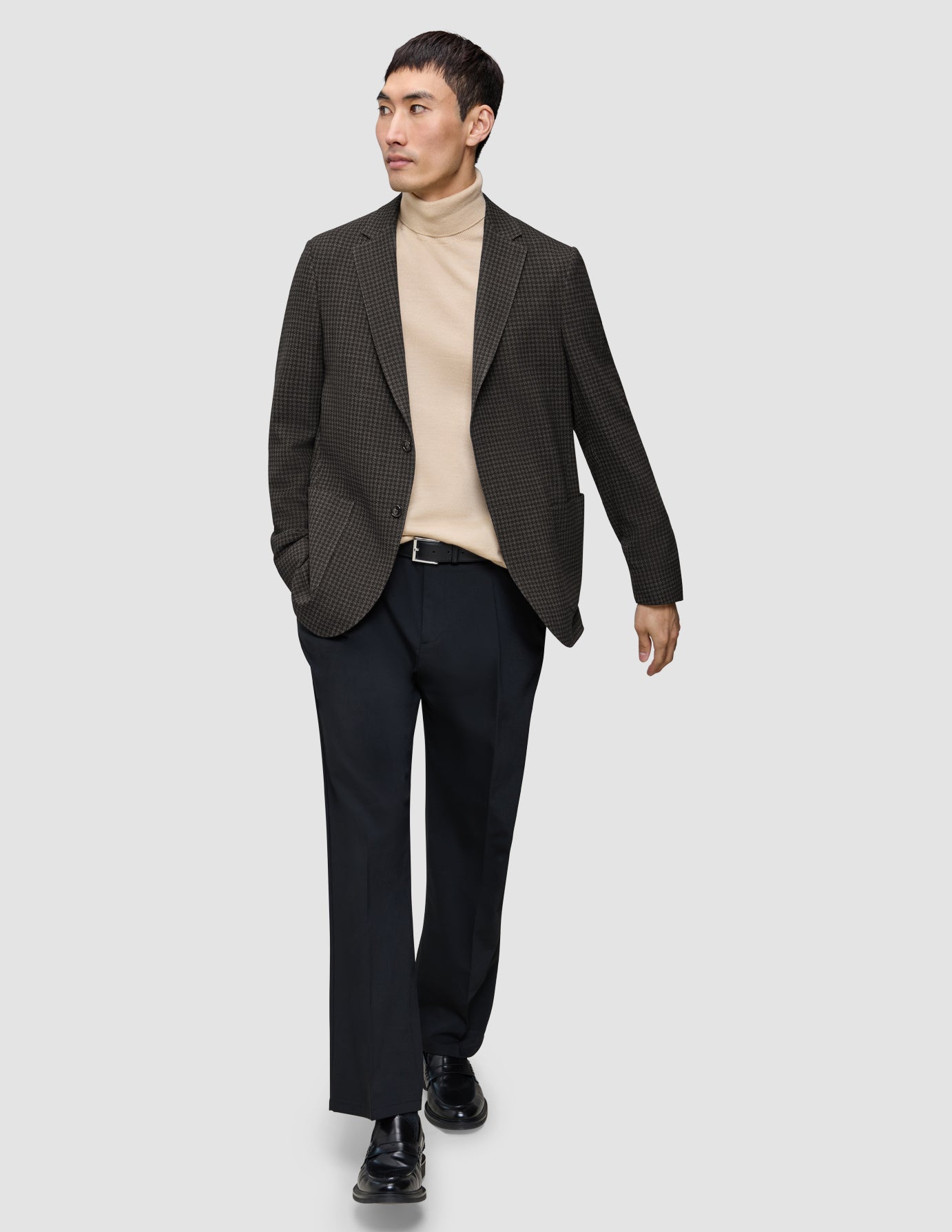 A person wears a Timeless Wool Blazer Slim Dark Brown Check over a tan turtleneck sweater, paired with black trousers and black loafers.