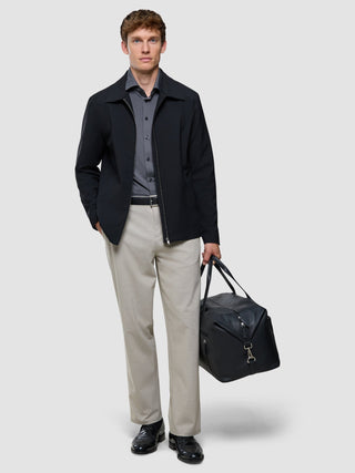 A man in a black jacket, Travel Shirt Charcoal Grey Regular, and tan trousers carries a black leather duffel bag.