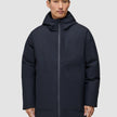 A man wears a black Utility Jacket Black with a hood that zips to the chin, featuring a vertical chest pocket and two large front pockets.