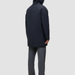 A person seen from behind wearing a black Utility Jacket Black hooded waterproof jacket, gray trousers, and black shoes.