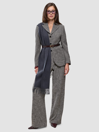 A woman wears a gray herringbone bouclé blazer, matching Women Ashryn Pants Wide Domino Herringbone, a dark blue scarf, a brown leather belt, and tinted glasses.