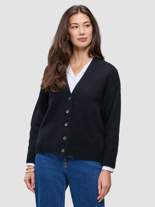 A person wears a Women Chunky Soft Wool Knit Cardigan Black over a white shirt and blue jeans.