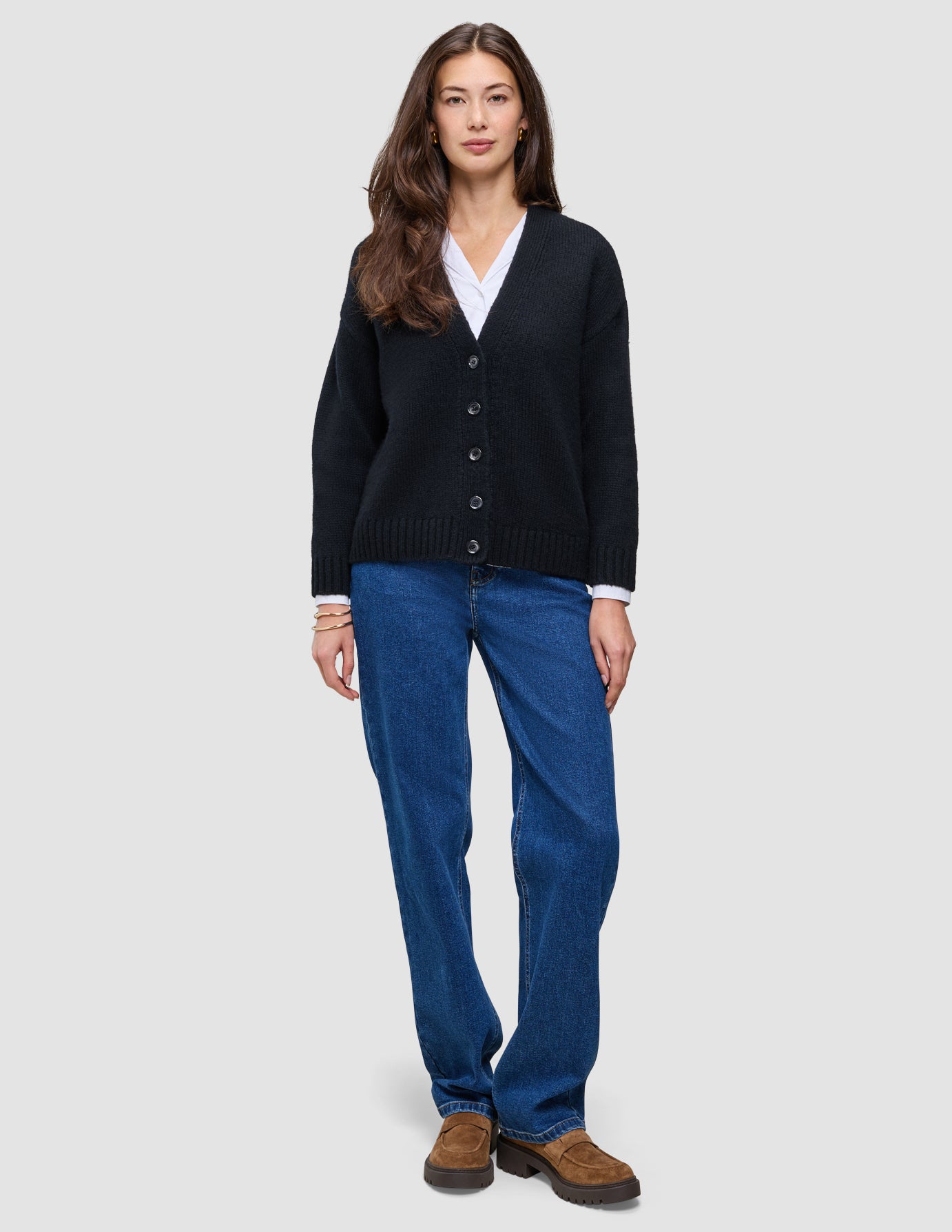 A woman wearing a Women Chunky Soft Wool Knit Cardigan Black over a white collared shirt, paired with blue jeans and brown loafers.