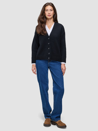 A woman wearing a Women Chunky Soft Wool Knit Cardigan Black over a white collared shirt, paired with blue jeans and brown loafers.