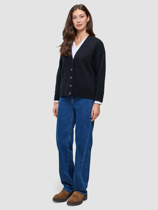 A woman wearing a Women Chunky Soft Wool Knit Cardigan Black over a white shirt, blue jeans, and brown loafers.