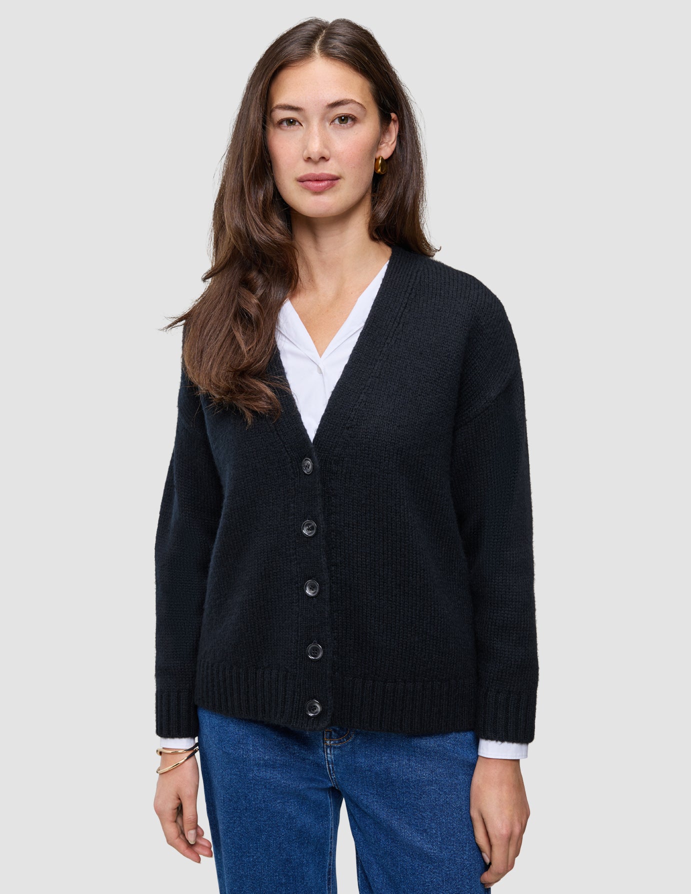 A woman wearing a black Women Chunky Soft Wool Knit Cardigan over a white shirt and blue jeans.