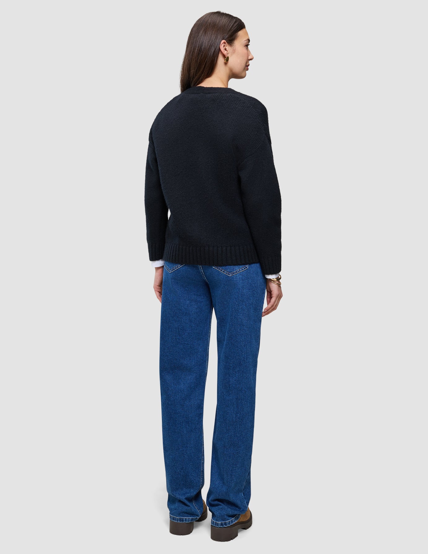 A woman seen from behind wearing a black Women Chunky Soft Wool Knit Cardigan over a white shirt and blue jeans.