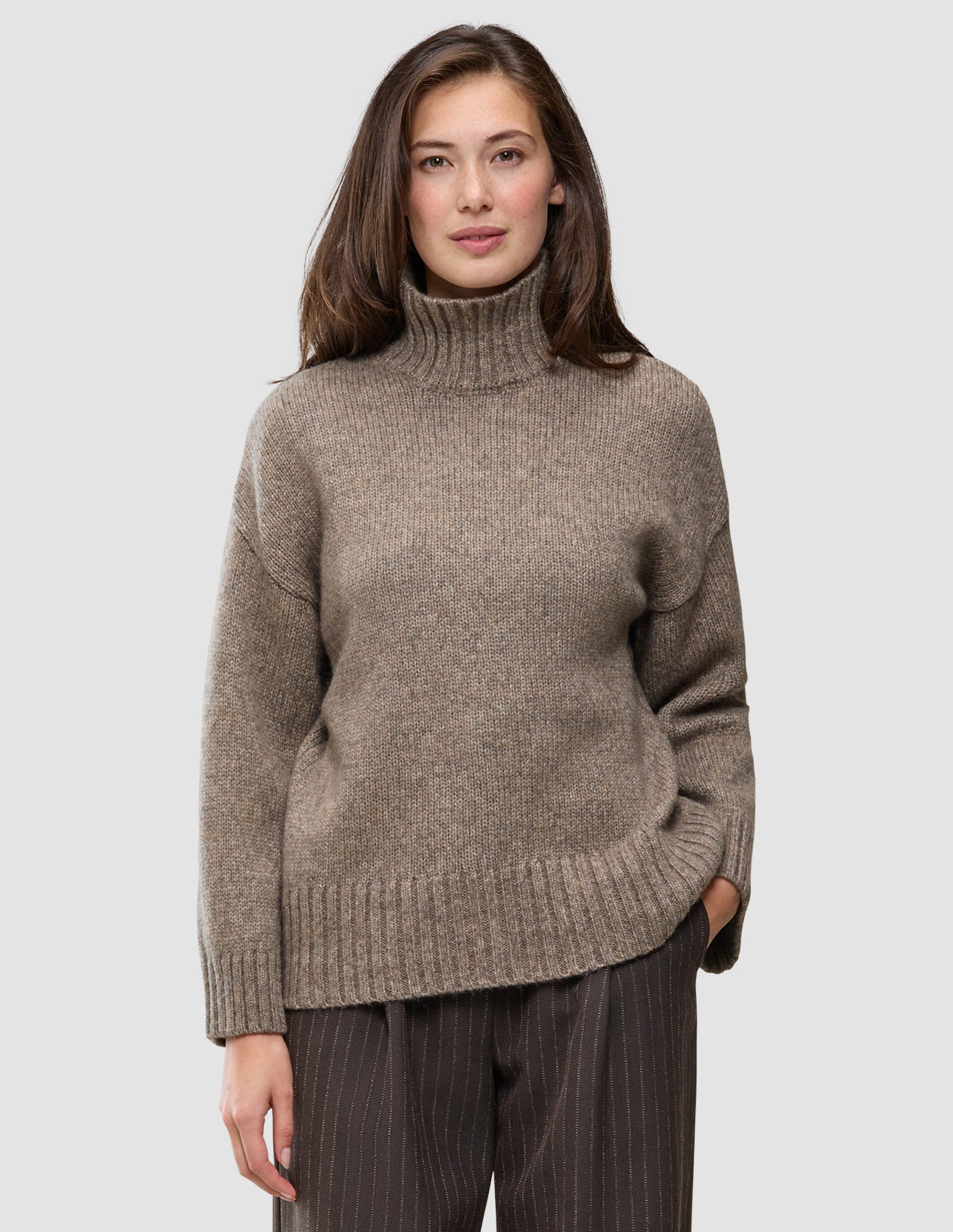 A woman wearing a Women Chunky Soft Wool Knit Turtleneck Taupe Melange, a taupe chunky knit turtleneck sweater in a Scandinavian design.