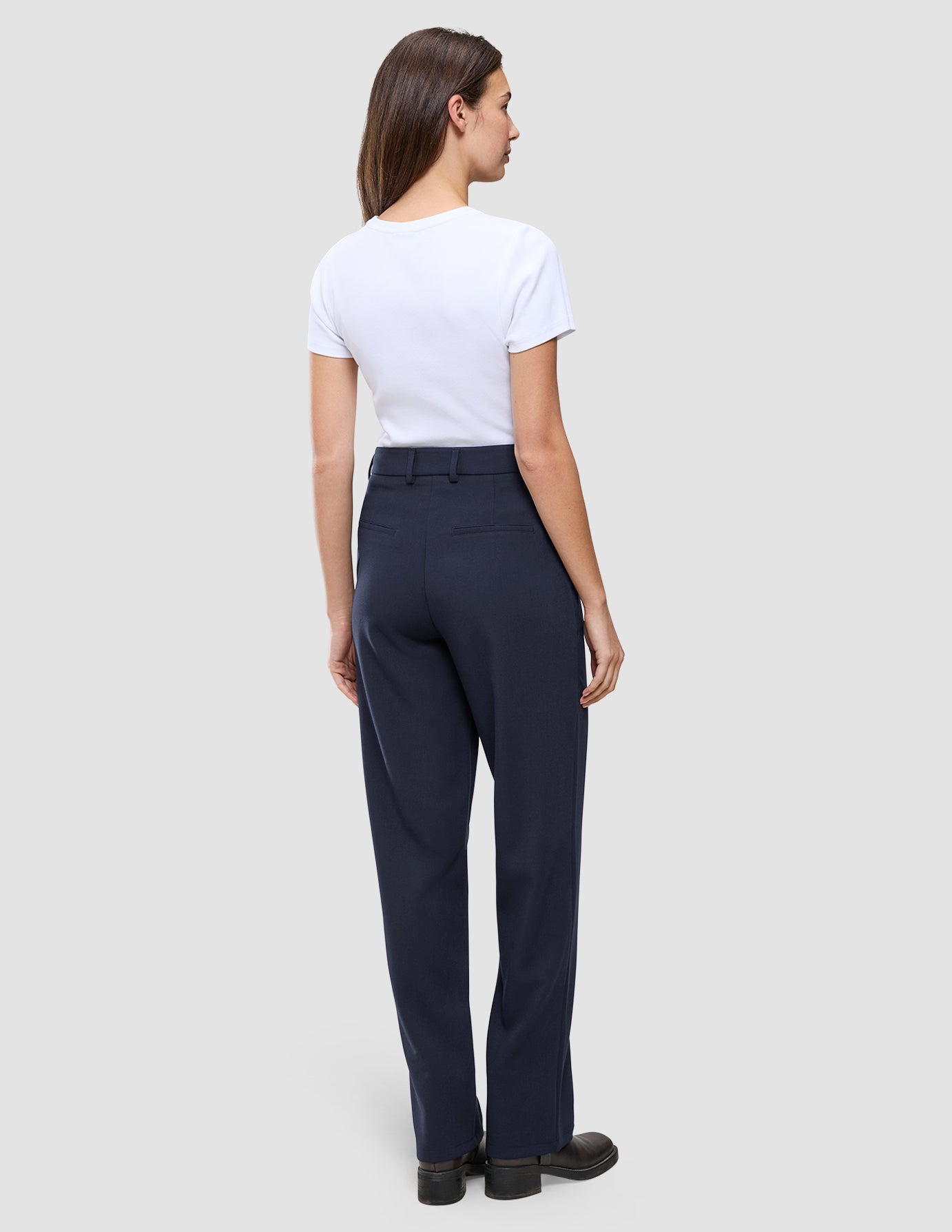 A woman seen from behind wearing a white t-shirt and Women GO2 Pants Straight Blue Nights, which are dark blue high-waisted, straight-leg trousers.