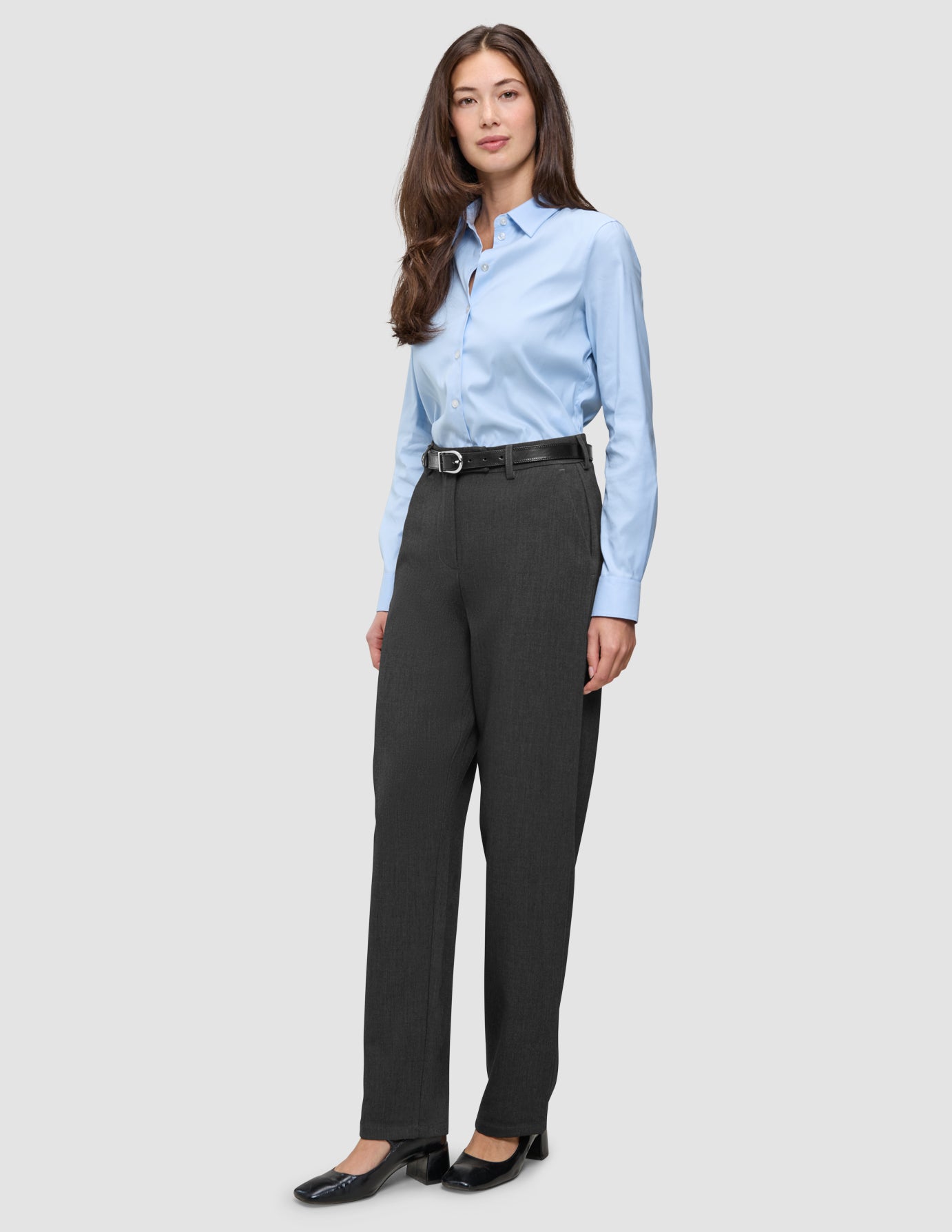 A woman wearing a light blue button-down shirt, a black belt, Women GO2 Pants Straight Dark Grey Melange, and black block-heel shoes.