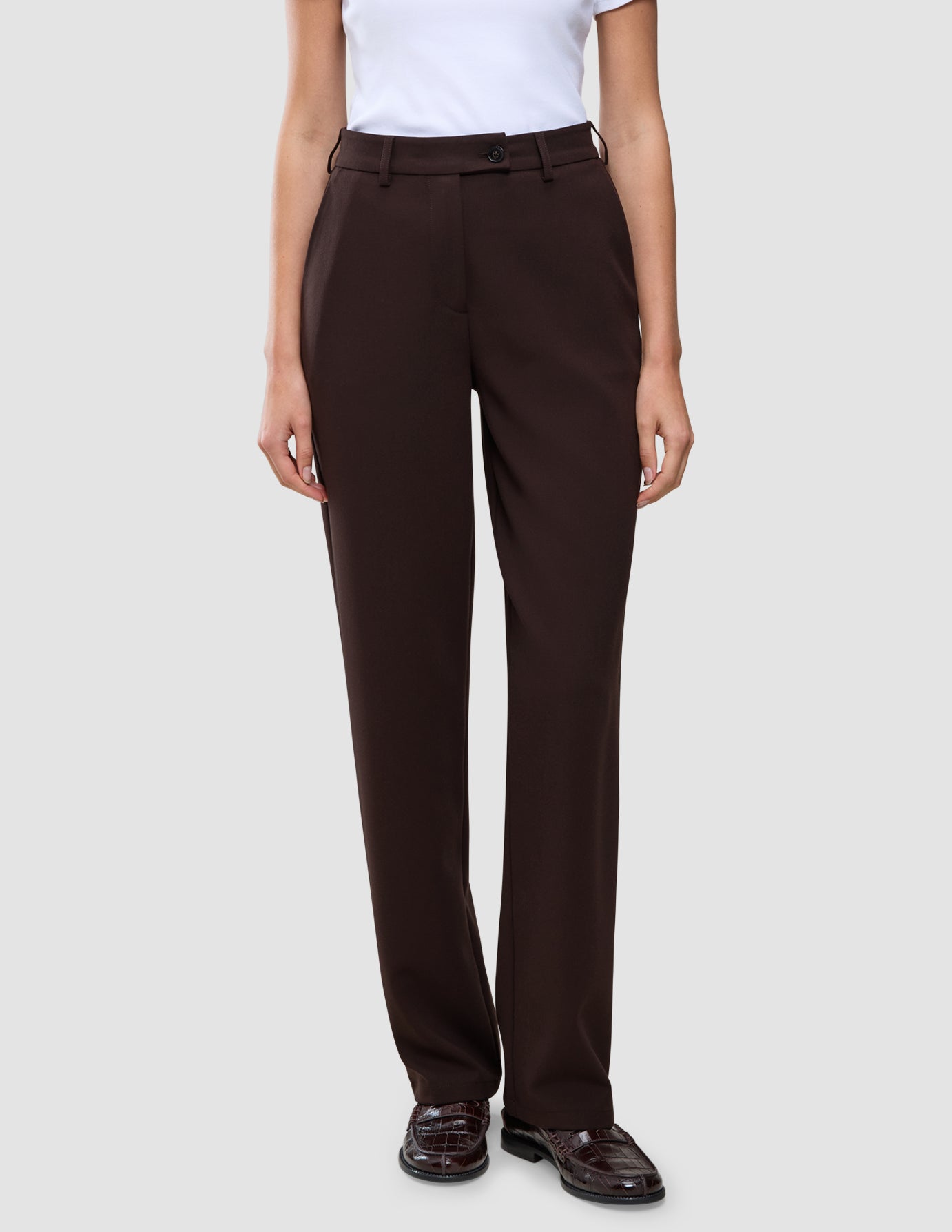 A person wearing Women GO2 Pants Straight Mocha high-waisted, dark brown straight-leg trousers and dark brown loafers.