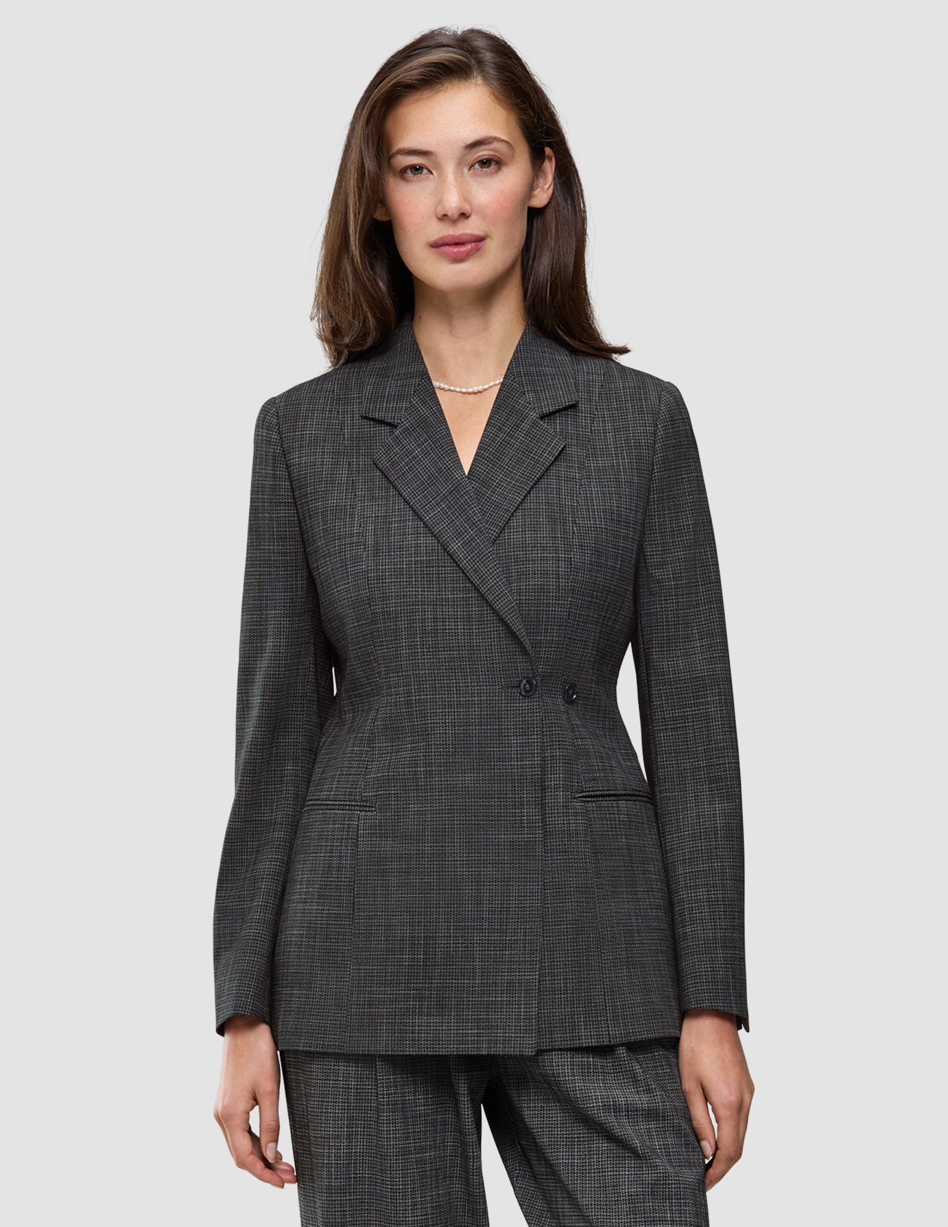 A woman wearing a Women Nara Blazer Fitted Black Check, a tailored, double-breasted blazer in a black-and-white checkered Scandinavian design.