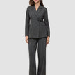 A woman wearing the Women Nara Blazer Fitted Black Check in charcoal gray plaid, paired with matching wide-leg trousers in a Scandinavian design.