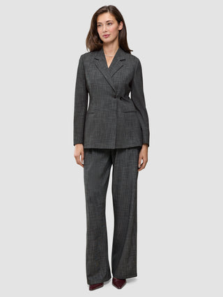 A woman wearing the Women Nara Blazer Fitted Black Check in charcoal gray plaid, paired with matching wide-leg trousers in a Scandinavian design.