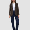 A woman wears a Women Serene Blazer Regular Walnut Herringbone over a white t-shirt, dark wash jeans, and brown heeled boots.