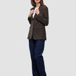 A person wears a Women Serene Blazer Regular Walnut Herringbone over a white t-shirt and blue jeans.