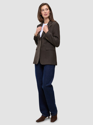 A person wears a Women Serene Blazer Regular Walnut Herringbone over a white t-shirt and blue jeans.